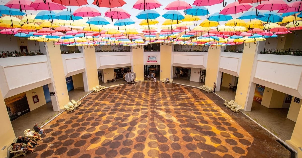 Interior of the Puerto Mágico complex with colorful Mexican umbrellas hanging from the ceiling and a wide geometric patterned floor, where cruise passengers step inside