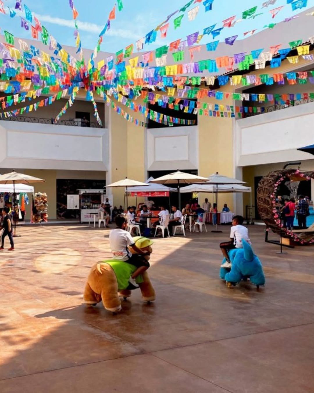 Plaza de Puerto Mágico decorada con papel picado de colores, sombrillas y personajes animados para familias durante un evento cultural